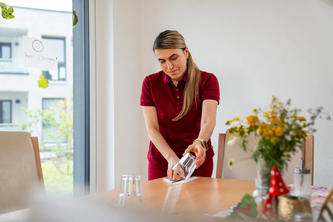 Cardia-Mitarbeiterin reinigt einen Tisch im Gemeinschaftsraum der Springbachhöfe